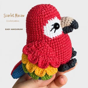 May include: A crocheted Scarlet Macaw amigurumi toy featuring a bright red head and body, a white face patch, a black eye, a beige and black beak, and layered wings in yellow, green, and blue. The text Scarlet Macaw Crochet pattern EASY AMIGURUMI is visible.