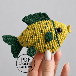 Peut inclure: Un petit poisson en crochet fait main avec un corps jaune vif parsemé de taches vert foncé, une nageoire dorsale, une queue et une nageoire pectorale vert foncé. Le poisson possède un œil en plastique noir et le texte PDF CROCHET PATTERN.