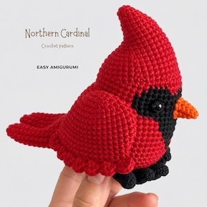May include: A red and black crocheted Northern Cardinal amigurumi bird with an orange beak and black eyes. The text Northern Cardinal Crochet pattern EASY AMIGURUMI is visible in the upper left corner of the image.