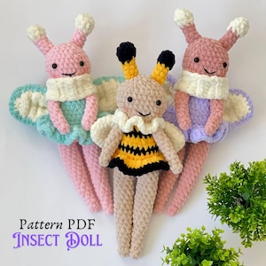 May include: Three handmade crochet insect dolls. The dolls have smiling faces, antennae, and wings. One doll is a bee with a yellow and black dress. The other two dolls are butterflies, one pink and one purple. The text "Pattern PDF INSECT DOLL" is at the bottom.