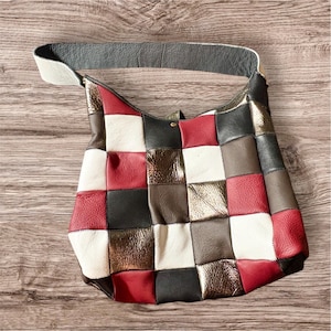 Peut inclure: Un sac à bandoulière patchwork avec une sangle grise et un design multicolore. Le sac présente des carrés de cuir rouge, blanc, noir, marron et or métallique. Le sac est en cuir et possède une fermeture à bouton.