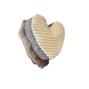 Puede incluir: Un cojín en forma de corazón con una combinación de texturas. Cuenta con una suave tela crema acanalada en un lado, una tela gris en el medio y un ribete de piel sintética marrón. El cojín está diseñado para fines decorativos.