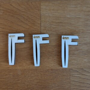 Peut inclure: Trois petits outils en bois de couleur claire, de conception unique en forme de F. Chaque outil porte une mesure de 4 mm. Les outils sont disposés sur une surface en bois.