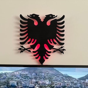 Könnte beinhalten: Eine schwarze Silhouette eines Doppelkopfadels mit roter Beleuchtung dahinter. Der Adler ist ein Symbol Albaniens.