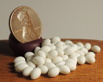 May include: A copper penny stands upright in a small, dark purple container, surrounded by a scattering of white, oval-shaped candies. The candies are on a wooden surface, with a neutral background.