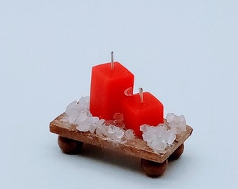 May include: A miniature wooden tray with two red candles and small white crystals. The candles have silver wicks and are different sizes. The tray has four small, round, brown feet.