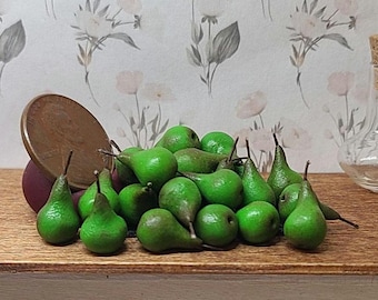 May include: A collection of miniature green pears with brown stems piled together next to a copper penny for scale. The small, realistic fruit replicas are arranged in a cluster, showcasing their smooth, rounded shapes and vibrant green color.