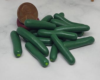 May include: A collection of miniature, hand-painted green zucchini vegetables. A U.S. penny is included for scale. The zucchini are a vibrant green color and appear to be made of clay or a similar material. The miniature vegetables are likely for a dollhouse or craft project.