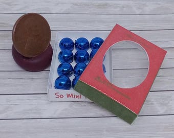 May include: A collection of miniature blue spheres in a white box, with the text "So Mini". A red card with a circular cutout and green trim is positioned next to the box. A brown disc sits atop a purple object.