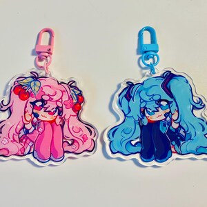 Pu&ograve; includere: Due ciondoli in acrilico con illustrazioni di personaggi in stile anime. Uno &egrave; rosa con ciliegie, l'altro blu. Ogni ciondolo ha una chiusura colorata. Adatto per portachiavi.