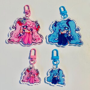 Pu&ograve; includere: Quattro portachiavi in acrilico con personaggi in stile anime. Due portachiavi hanno capelli rosa e dettagli di ciliegie, attaccati a chiusure rosa. Gli altri due hanno i capelli blu e sono attaccati a chiusure blu. Tutti hanno un contorno bianco.