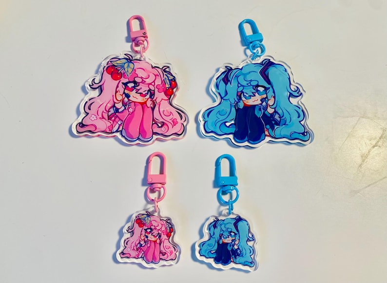 Pu&ograve; includere: Quattro portachiavi in acrilico con personaggi in stile anime. Due portachiavi hanno capelli rosa e dettagli di ciliegie, attaccati a chiusure rosa. Gli altri due hanno i capelli blu e sono attaccati a chiusure blu. Tutti hanno un contorno bianco.