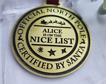 May include: Gold-colored round ornament with the text "Official North Pole Certified by Santa" and "Alice is on the Nice List" with a star and a reindeer graphic.