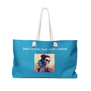 May include: A large turquoise tote bag with white rope handles. The bag features the text "Dead inside but caffeinated" above an illustration of a skeleton holding a coffee cup. The skeleton has blue hair and is wearing makeup.