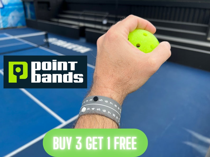 Pode incluir: Um bra&ccedil;o usando uma pulseira Point Bands cinza com n&uacute;meros brancos e um mostrador preto, segurando uma bola de pickleball verde neon. O logotipo Point Bands &eacute; vis&iacute;vel. O texto diz "BUY 3 GET 1 FREE".