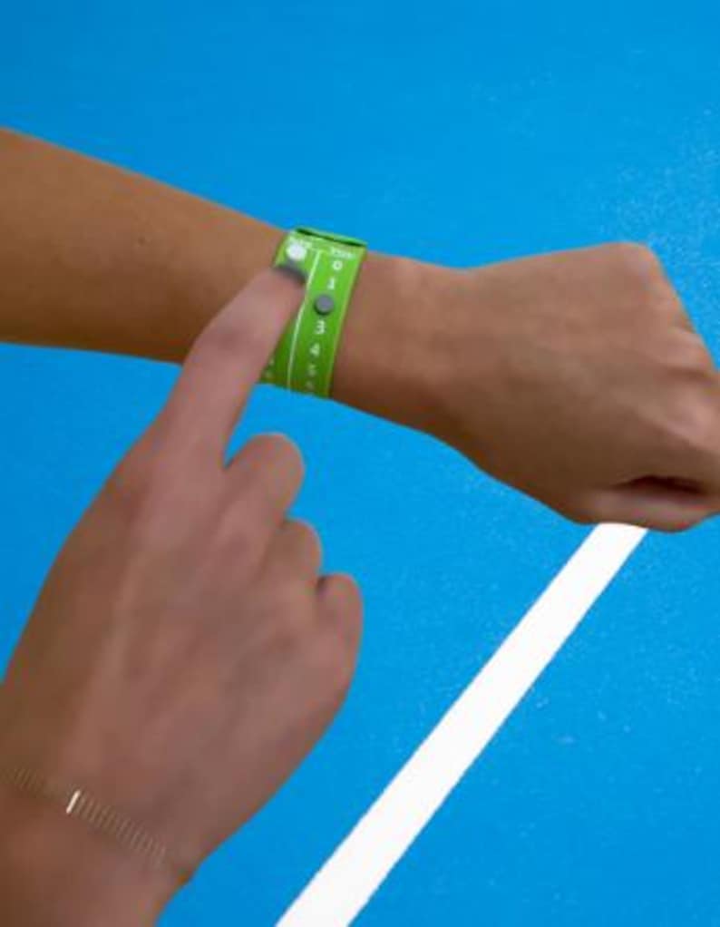 Pode incluir: Uma pulseira verde com n&uacute;meros brancos e fecho de bot&atilde;o &eacute; usada no pulso. Um dedo pressiona o bot&atilde;o. O fundo &eacute; azul com uma faixa branca. A pulseira parece ser um acess&oacute;rio esportivo ou para eventos.