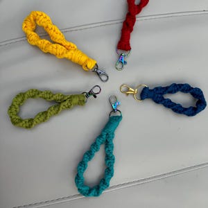 May include: Five colourful crocheted keychains with metal key rings. The keychains are red, yellow, green, blue and dark blue.