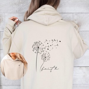Pu&ograve; includere: Una felpa con cappuccio beige con un disegno di dente di leone nero e la parola "faith" stampata sul retro.
