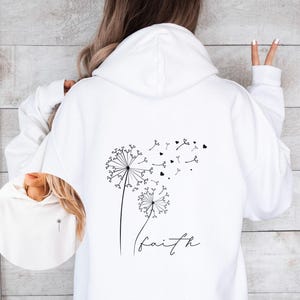 Pu&ograve; includere: Felpa bianca con un design a dente di leone nero e la parola "faith" stampata sul davanti.