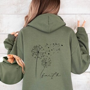 Pu&ograve; includere: Una felpa con cappuccio verde con un disegno di dente di leone nero e la parola "faith" stampata sul retro.