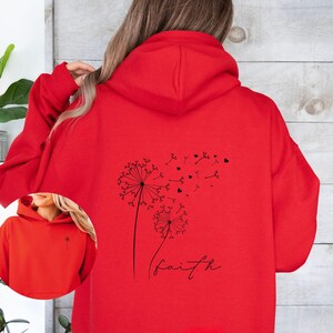 Pu&ograve; includere: Felpa con cappuccio rossa con un disegno di dente di leone nero e la parola "faith" stampata sul retro.
