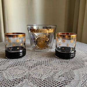 May include: Three vintage glass tumblers with gold and black accents. The tumblers have a snowflake pattern and are perfect for serving drinks.