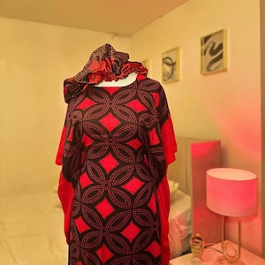 May include: A red and black patterned dress with a matching head wrap. The dress has a loose, flowing silhouette and a round neckline. The pattern is made up of small circles and diamonds.