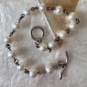 Peut inclure: Un bracelet délicat avec des perles blanches et une chaîne argentée. Le bracelet est doté d'un fermoir à bascule. Les perles sont espacées de manière uniforme, créant un look classique et élégant. Un bijou intemporel.