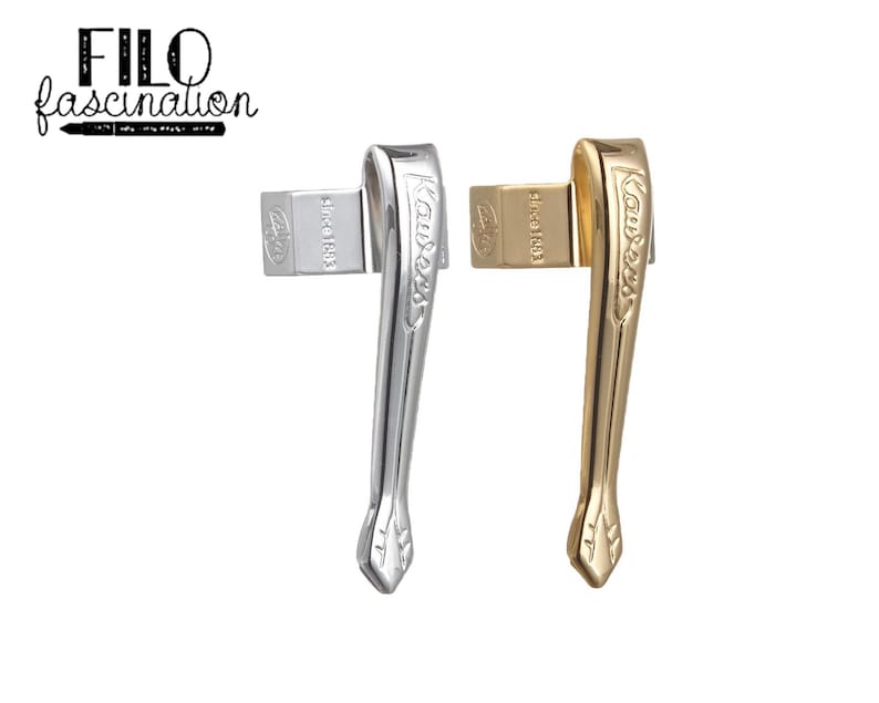 May include: Two pen clips, one silver and one gold, are displayed against a white background. The silver clip is on the left, and the gold clip is on the right. Each clip has a rectangular piece with the text "since 1883" and the brand name "Aurora" on the curved body.