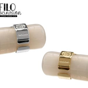 May include: Close-up of two pen clips, one silver and one gold, each encircling a cream-colored pen barrel. The silver clip is stamped with "KAWECO GERMANY". The gold clip also has "KAWECO GERMANY" stamped on it. The text "FILO fascination" is in the upper left corner.