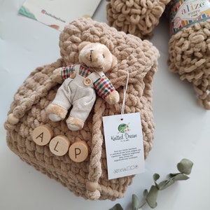 May include: A beige, knitted drawstring bag with wooden beads and the letters "ALP". A small teddy bear in overalls is attached to the bag. A ball of Alize Puffy Fine yarn and a tag with the "Knitted Dream" logo are also visible.
