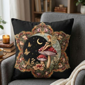 May include: Black decorative throw pillow featuring a fairy sitting on a mushroom, with butterflies and floral accents. The design includes a crescent moon and stars, framed by an ornate, gold-toned border. The pillow is placed on a gray armchair.