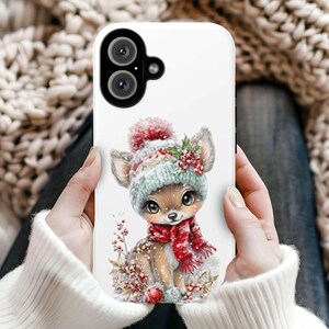 May include: White phone case featuring a watercolor illustration of a deer wearing a winter hat and scarf. The deer has large eyes and is surrounded by winter foliage. The case has a camera cutout.