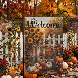 May include: A rectangular garden flag featuring the word Welcome in black script. The image displays a white picket fence adorned with sunflowers and autumn foliage, with a collection of orange and white pumpkins resting at the base.