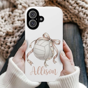 May include: White phone case featuring a volleyball design with a ribbon and hearts. The name "Allison" is written in a cursive font below the volleyball. The case has a camera cutout at the top.