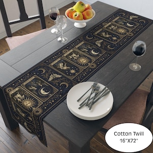 May include: A black table runner featuring a repeating pattern of celestial tarot-style cards with gold and white illustrations of suns, moons, stars, and moths. The runner is labeled as Cotton Twill measuring 16 inches by 72 inches in size.