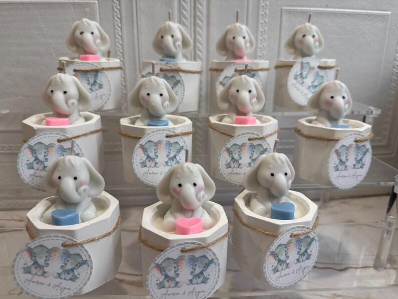 May include: A collection of white ceramic candle holders with elephant-shaped candles. Each holder features a small tag with two elephants and the text "Forever & Always".