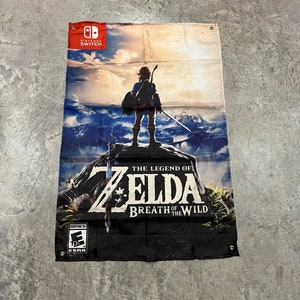 Könnte beinhalten: Ein schwarz-weißes Banner mit dem Text "The Legend of Zelda Breath of the Wild" und einer Videospielfigur, die auf einem Berggipfel steht. Das Banner hat oben links ein Nintendo Switch-Logo und unten links eine ESRB-Bewertung von "Everyone 10+".