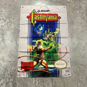 以下が含まれることがあります： 筋肉質なキャラクターがムチを振り回し、青い肌の悪魔と城が描かれた、長方形のキャッスルヴァニアのバナー。バナーにはコナミと任天堂のロゴと「Castlevania」の文字が入っています。バナーはグレーと白です。