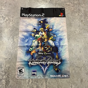 Puede incluir: Un póster del videojuego Kingdom Hearts con un grupo de personajes del juego, incluyendo Sora, Riku, Kairi, Donald Duck, Goofy y Mickey Mouse. El póster es azul, blanco y negro con el logotipo del juego y las palabras "PlayStation 2", "Disney", "Square Enix" y "Square Enix" en él.
