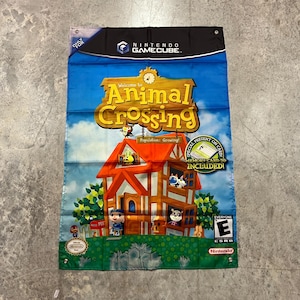 May include: A Nintendo GameCube banner for "Animal Crossing." The banner features a vibrant illustration of a house with characters, set against a blue sky. The game's title is prominently displayed in a large, golden font.