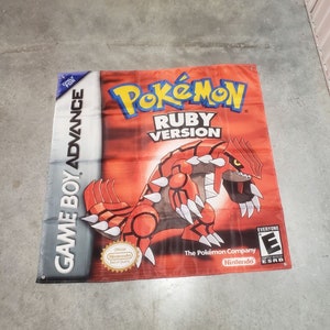 Op de afbeelding: Een rood-zwarte vlag met een Game Boy Advance-spelcartridge van Pokemon Ruby Version. De vlag toont een rood-zwart Pokemon-wezen met scherpe klauwen en tanden. De vlag toont ook de tekst "Pokemon Ruby Version" en het Game Boy Advance-logo.