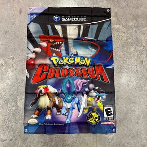 May include: A rectangular banner featuring the "Pokémon Colosseum" video game. The banner displays the Nintendo GameCube logo and various Pokémon characters in vibrant colors. The text "Pokémon Colosseum" is prominently displayed.