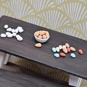 May include: A dark brown wooden table with a white bowl filled with brown eggs. There are also white and multi-colored eggs scattered on the table.