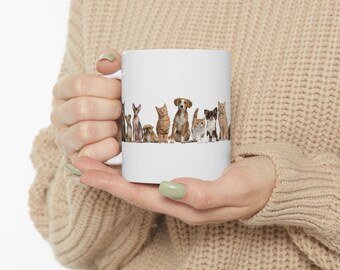 Könnte beinhalten: Weiße Keramiktasse mit einem bunten Bild einer Reihe von Katzen und Hunden, die in einer Reihe sitzen. Die Tiere sind alle verschiedenen Rassen und Farben.