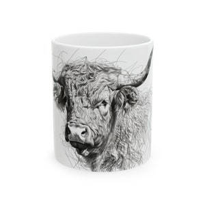 May include: A white ceramic mug with a black and white illustration of a Highland cow's head. The cow has a long, shaggy mane and a large, prominent nose.