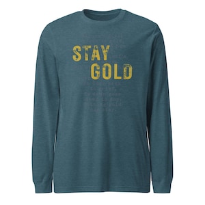 May include: A teal long-sleeve shirt with the words "STAY GOLD" in a distressed yellow font. The shirt also features a poem in a smaller font. The shirt is made of a soft material.
