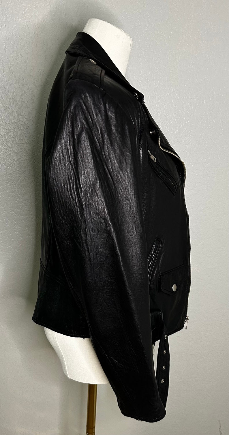 May include: A black leather motorcycle jacket with a zipper closure and a belt at the waist.