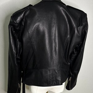 May include: Black leather jacket with a belted waist and zippered pockets. The jacket has a slightly oversized fit and features exaggerated shoulder pads.