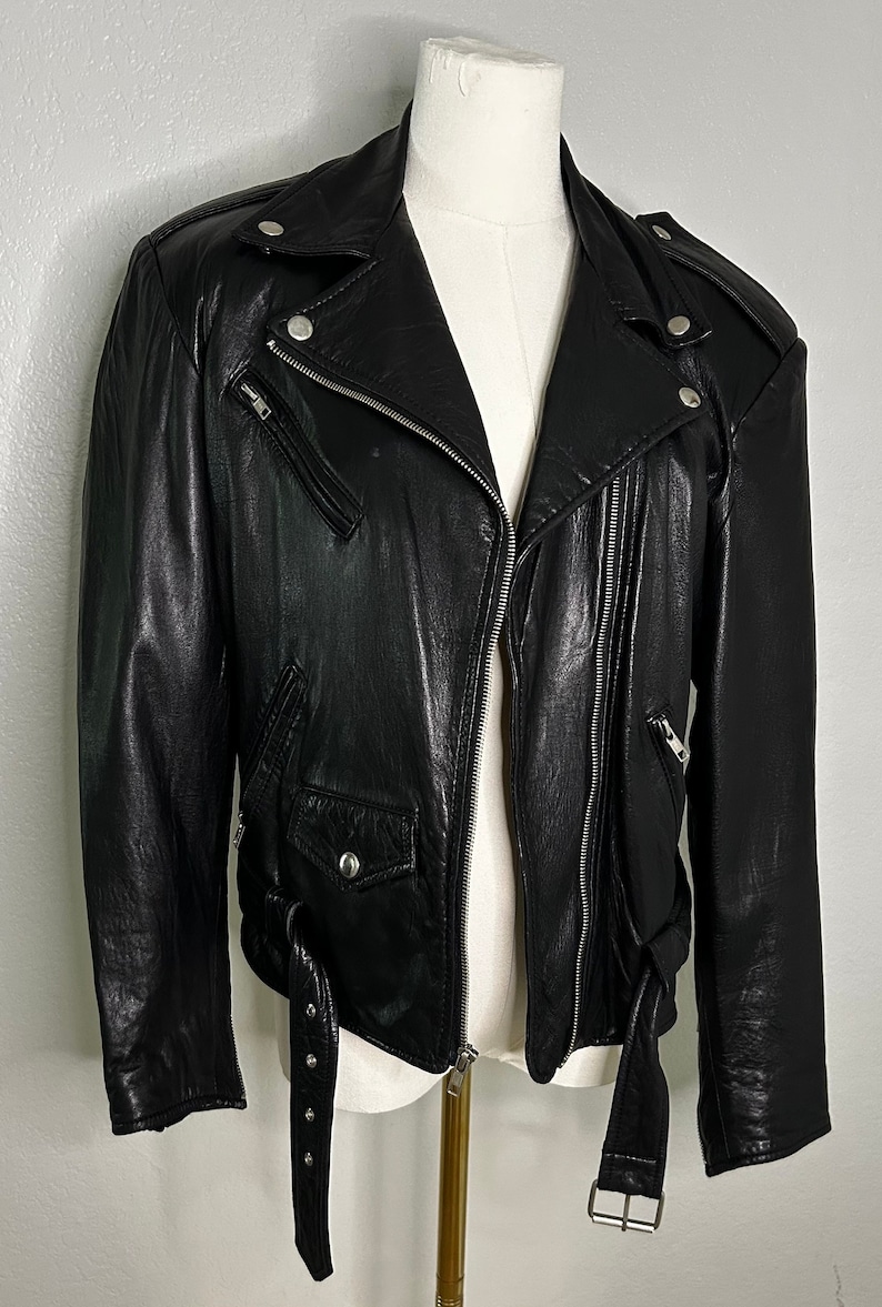 May include: A black leather motorcycle jacket with a zipper closure, two front pockets, and a belt with silver studs.